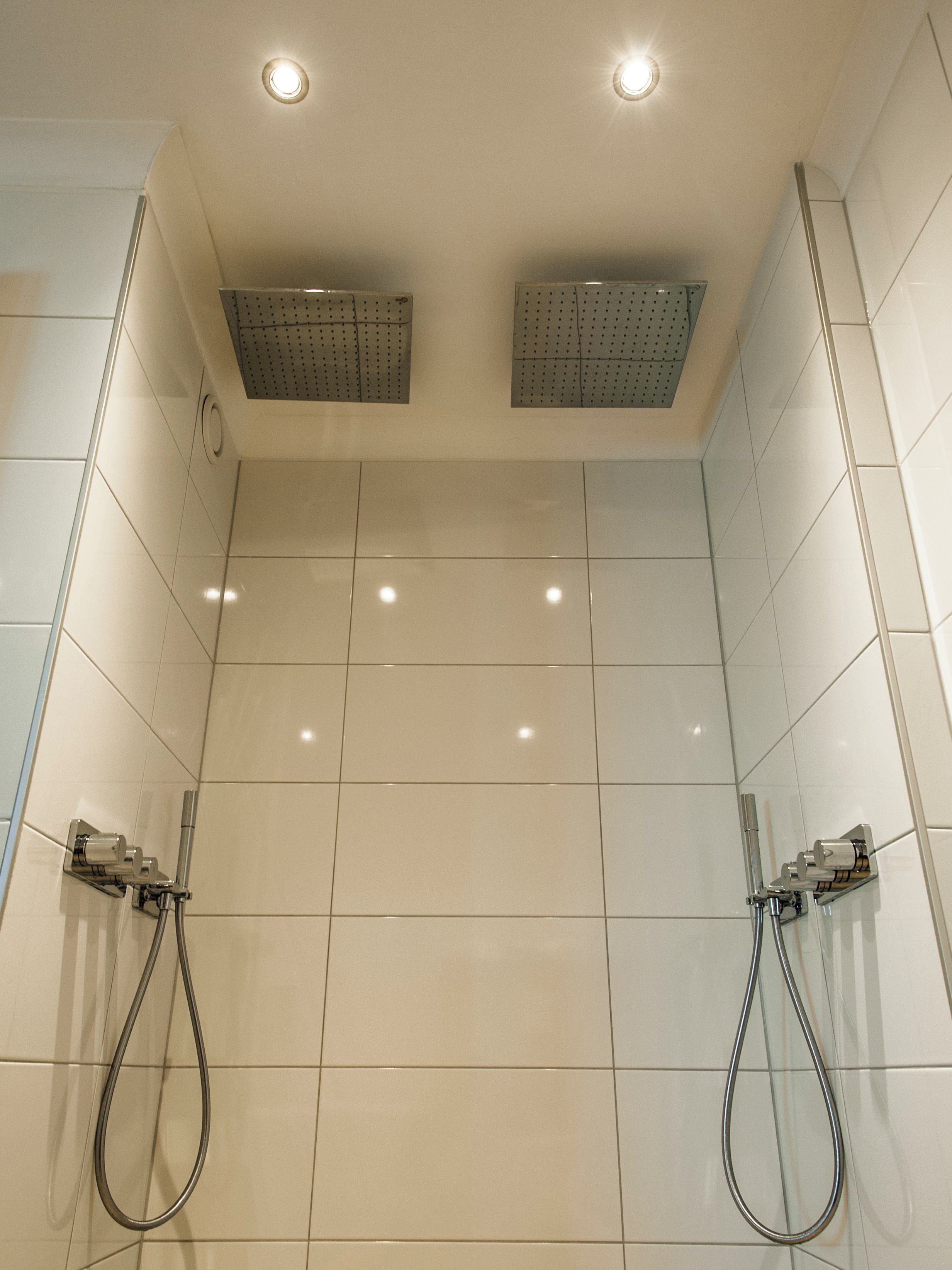 A bathroom with two showerheads, a ceiling light, and tiled walls.