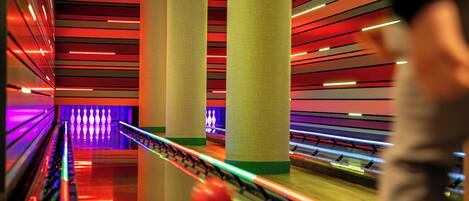 A bowling alley with multiple lanes, a bowling ball in motion, and a person in the foreground.