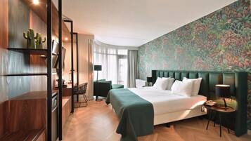 A hotel room with a large bed, a desk, a chair, a nightstand, and a wall with a floral pattern.