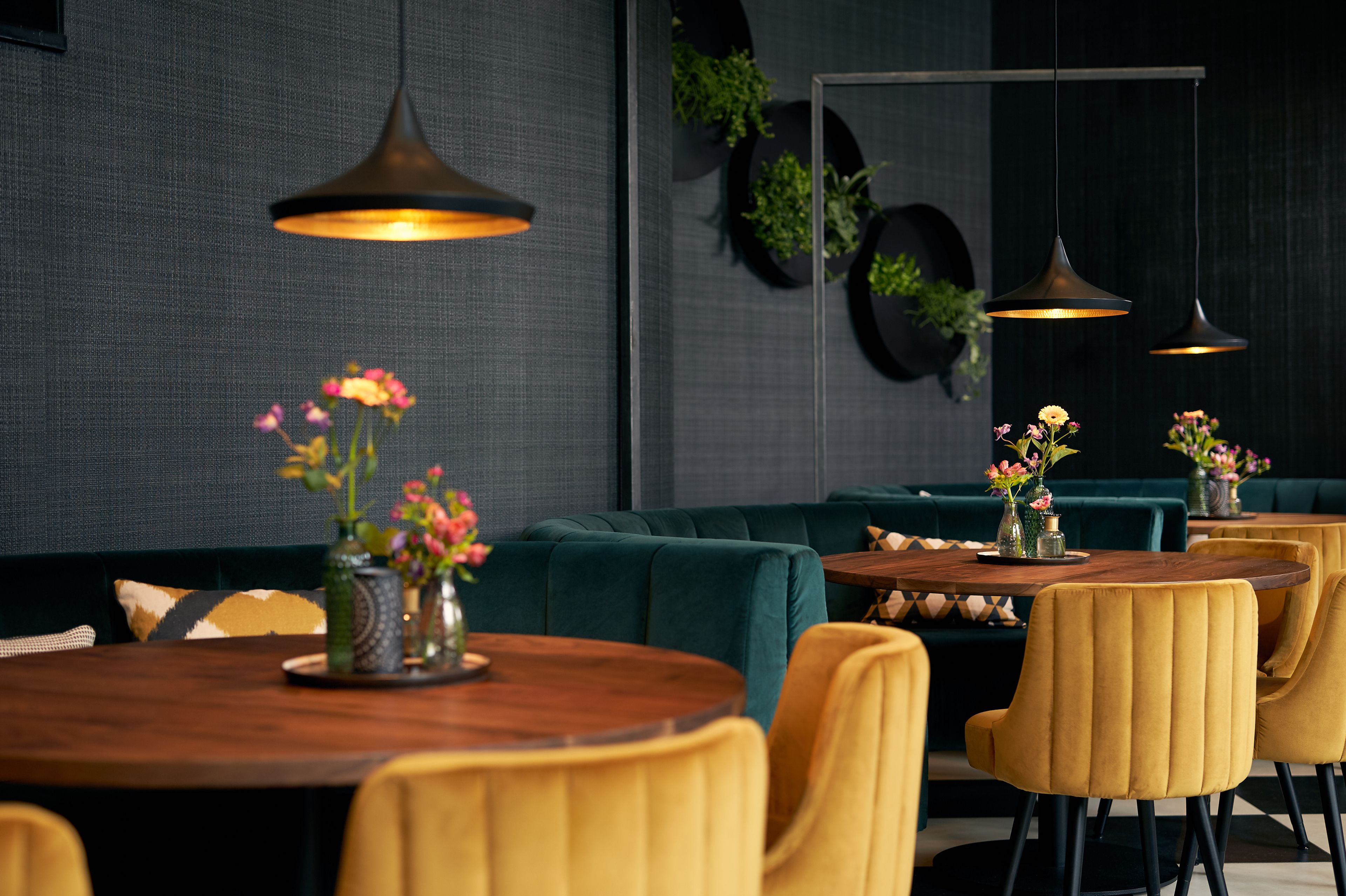 Un comedor moderno con asientos tapizados en verde oscuro, sillas amarillas y mesas de madera.