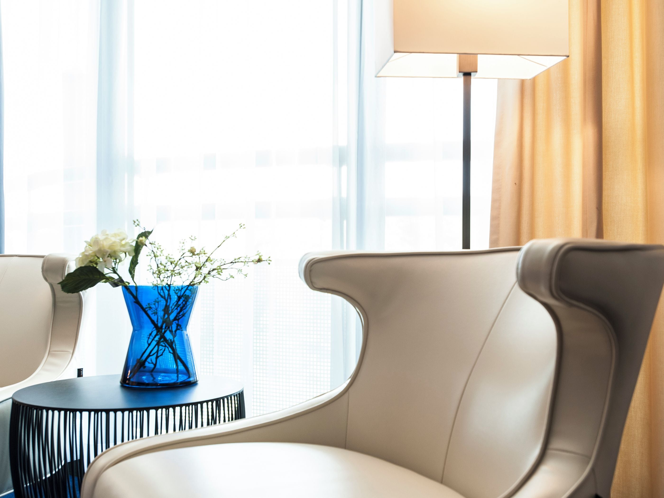 Ein modernes Zimmer mit einem weißen, gebogenen Sessel, einer blauen Vase mit Blumen und einer Lampe.