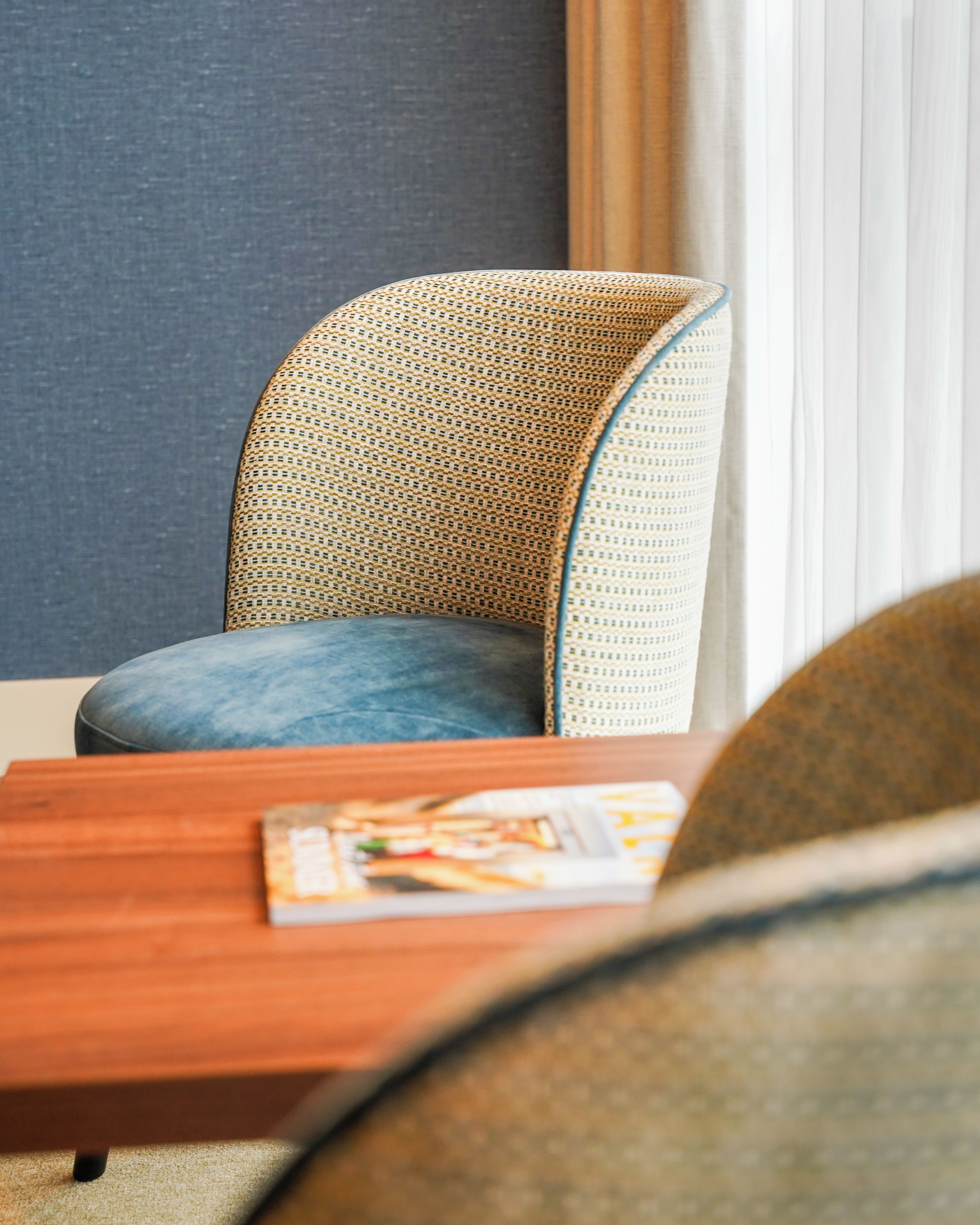 Une chaise dotée d’un dossier en osier et d’un coussin, placée à côté d’une table en bois sur laquelle se trouve un magazine.