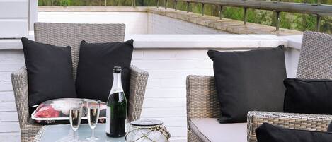 Un área de estar al aire libre con muebles de mimbre, una mesa, una botella y un vaso.