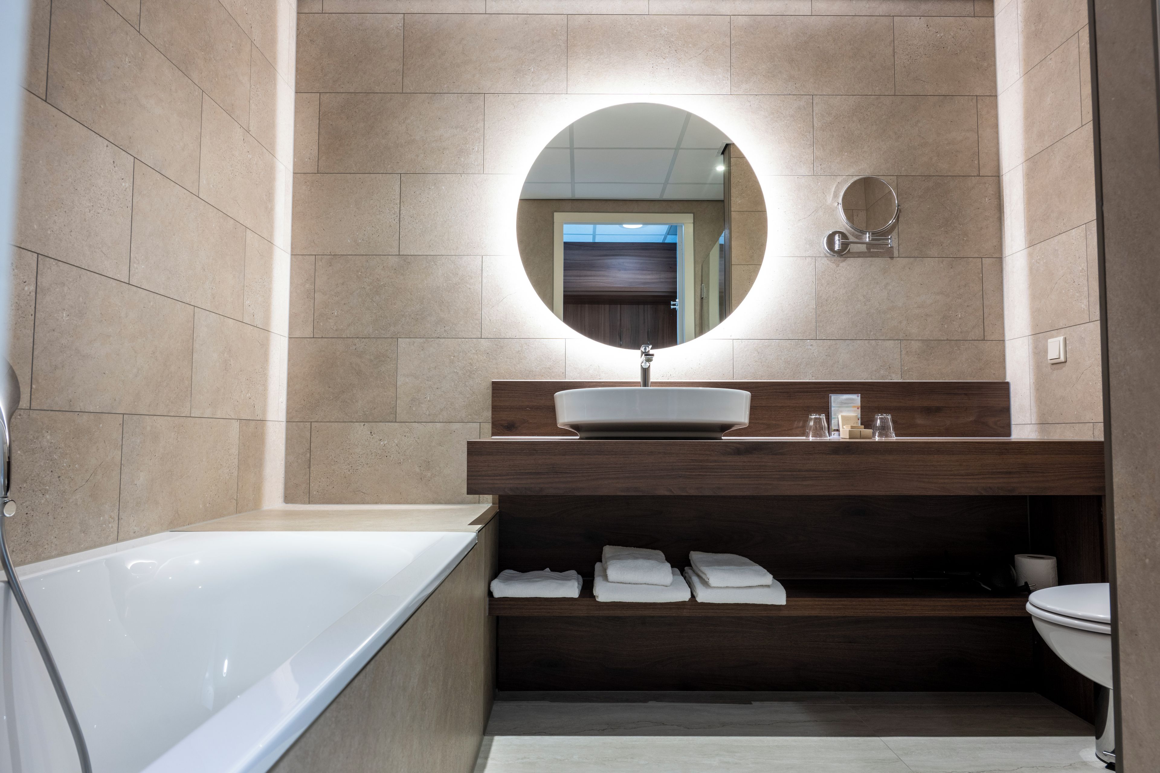 A modern bathroom with a freestanding bathtub, a round mirror, and a wooden vanity.