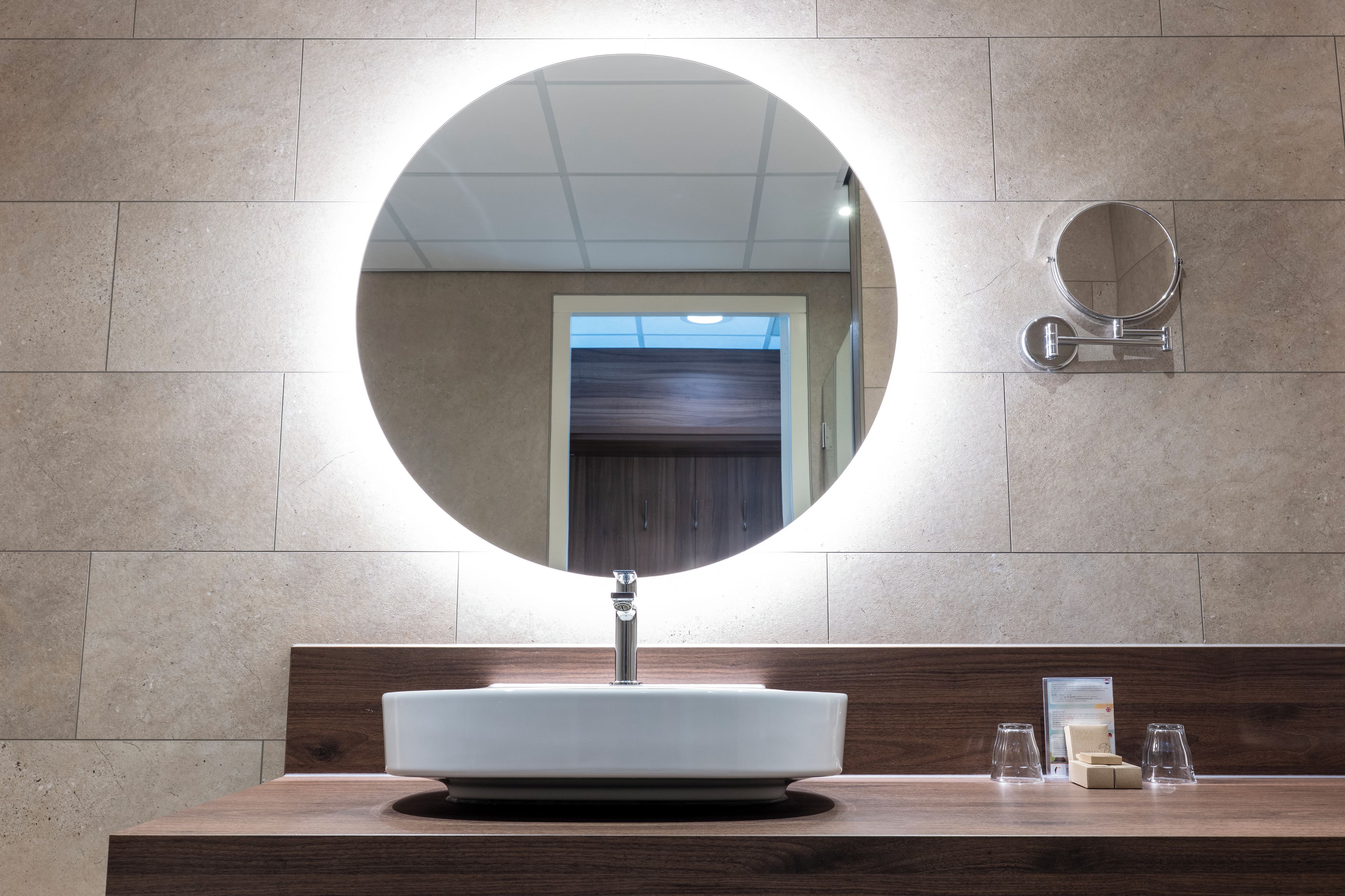A bathroom with a round mirror, a white sink, and a wooden vanity.