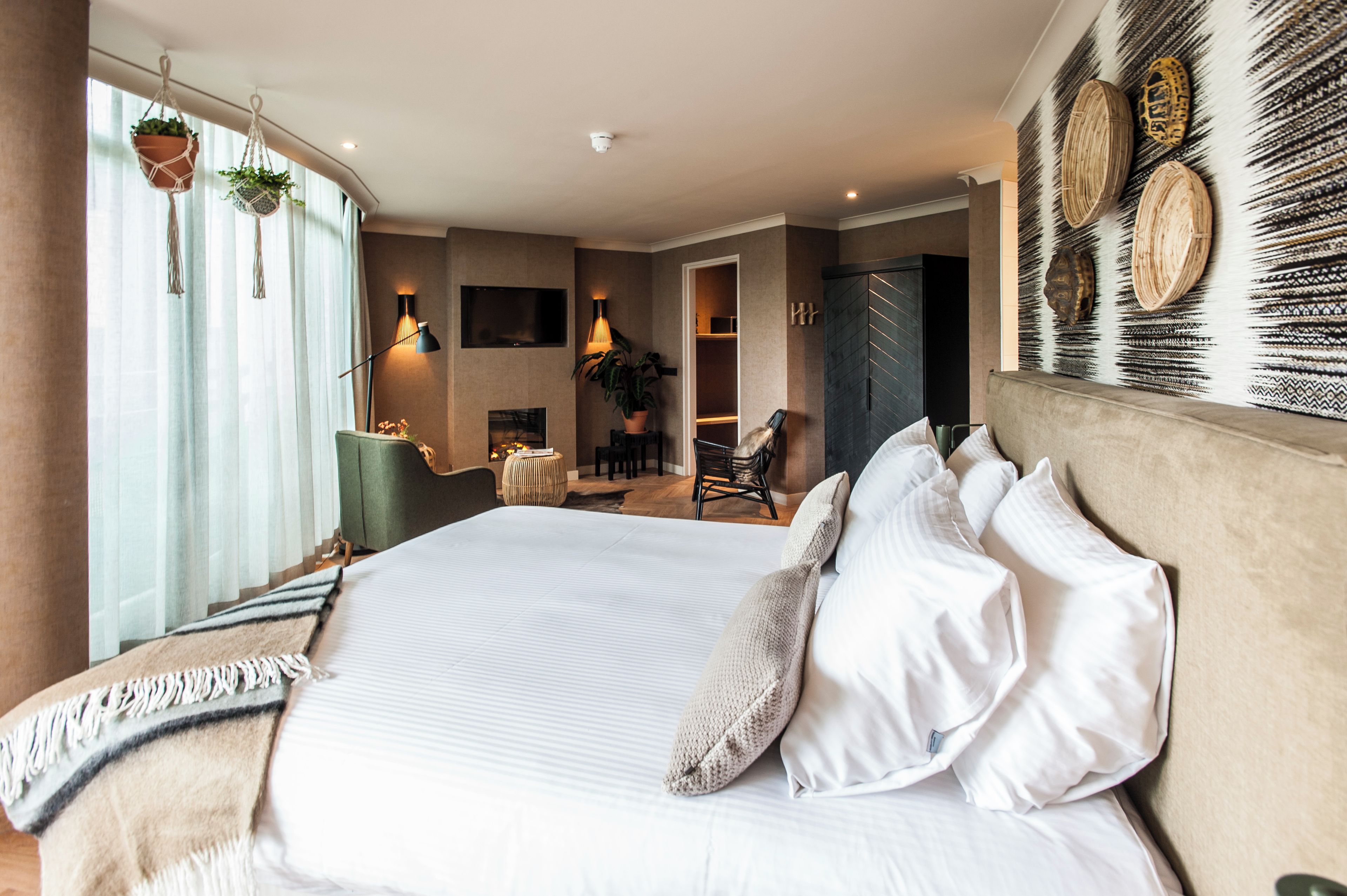 A modern hotel room with a large bed, a seating area with a chair and a table, and a television mounted on the wall.