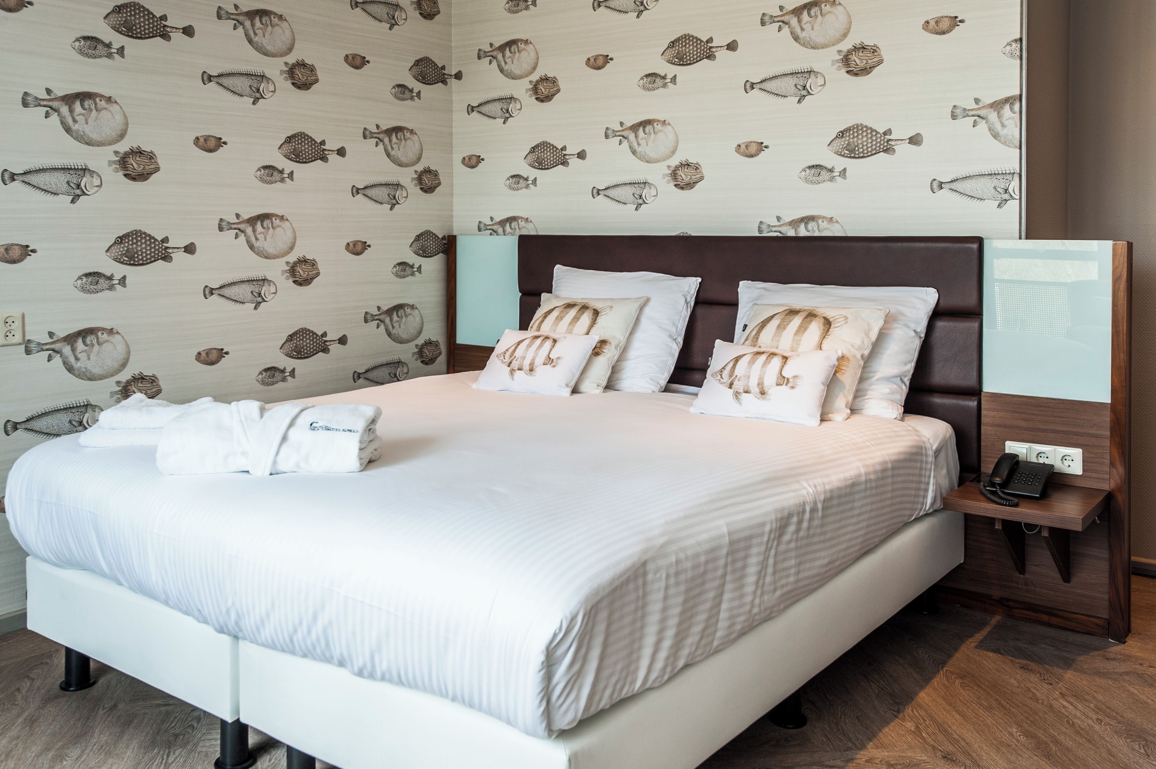 A hotel room with a bed, pillows, a bedside table with a phone, and a wall with fish patterns.