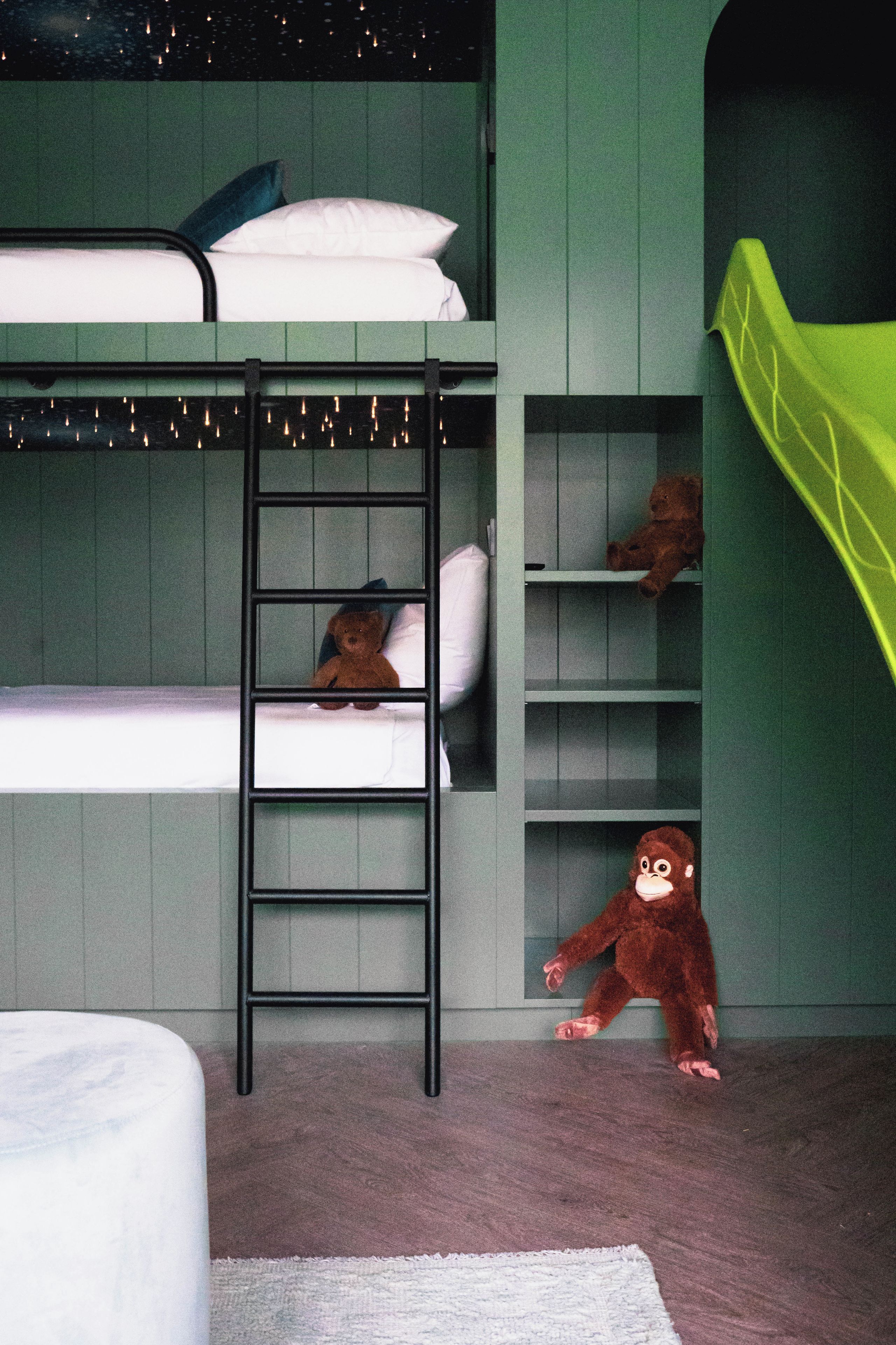 Una cama litera con escalera, un oso de peluche y una figura de mono en el suelo.