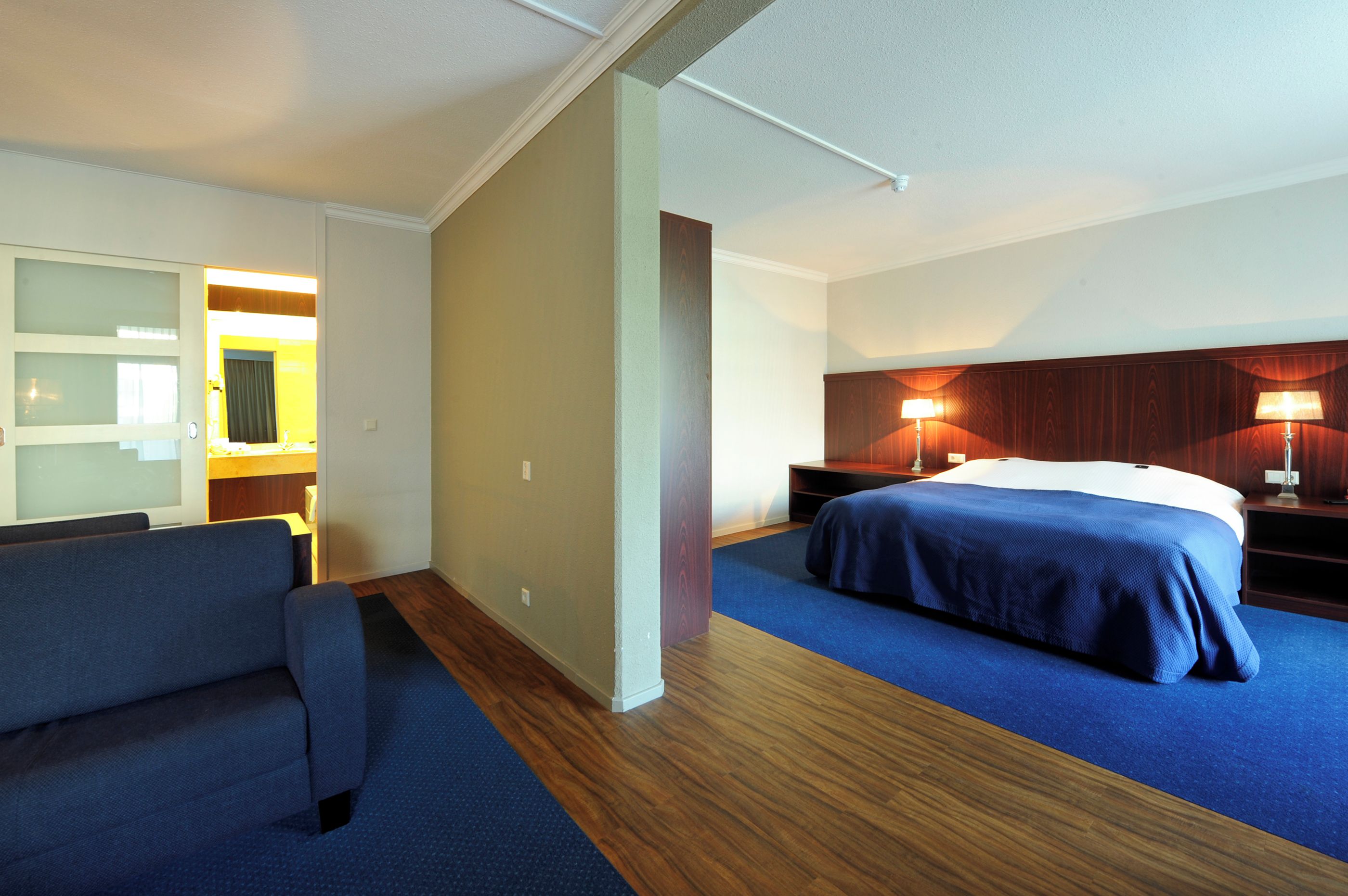 Una habitación de hotel con cama, sofá, mesita de noche y lámpara.