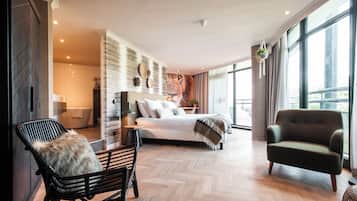 Un dormitorio moderno con una cama grande, una zona de estar con sillones y vistas al exterior a través de amplios ventanales.