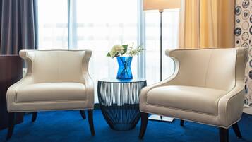 Een hotelkamer met twee fauteuils, een bijzettafeltje met een bloevas, een vloerlamp en een uitzicht op de stad door grote ramen.