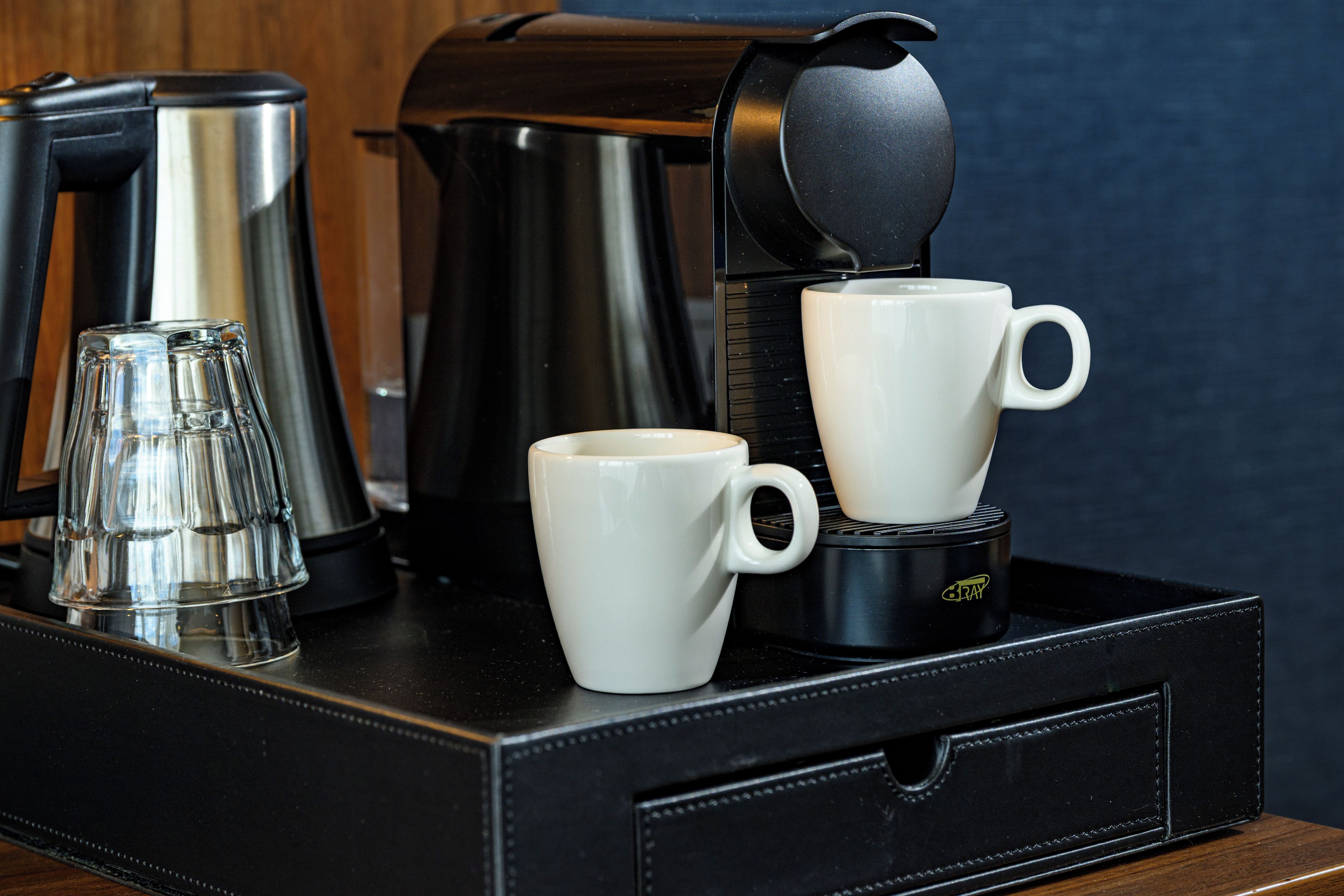 Une machine à café, deux tasses blanches et un verre sur un plateau.