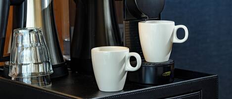 A coffee maker, two white cups, and a glass on a tray.