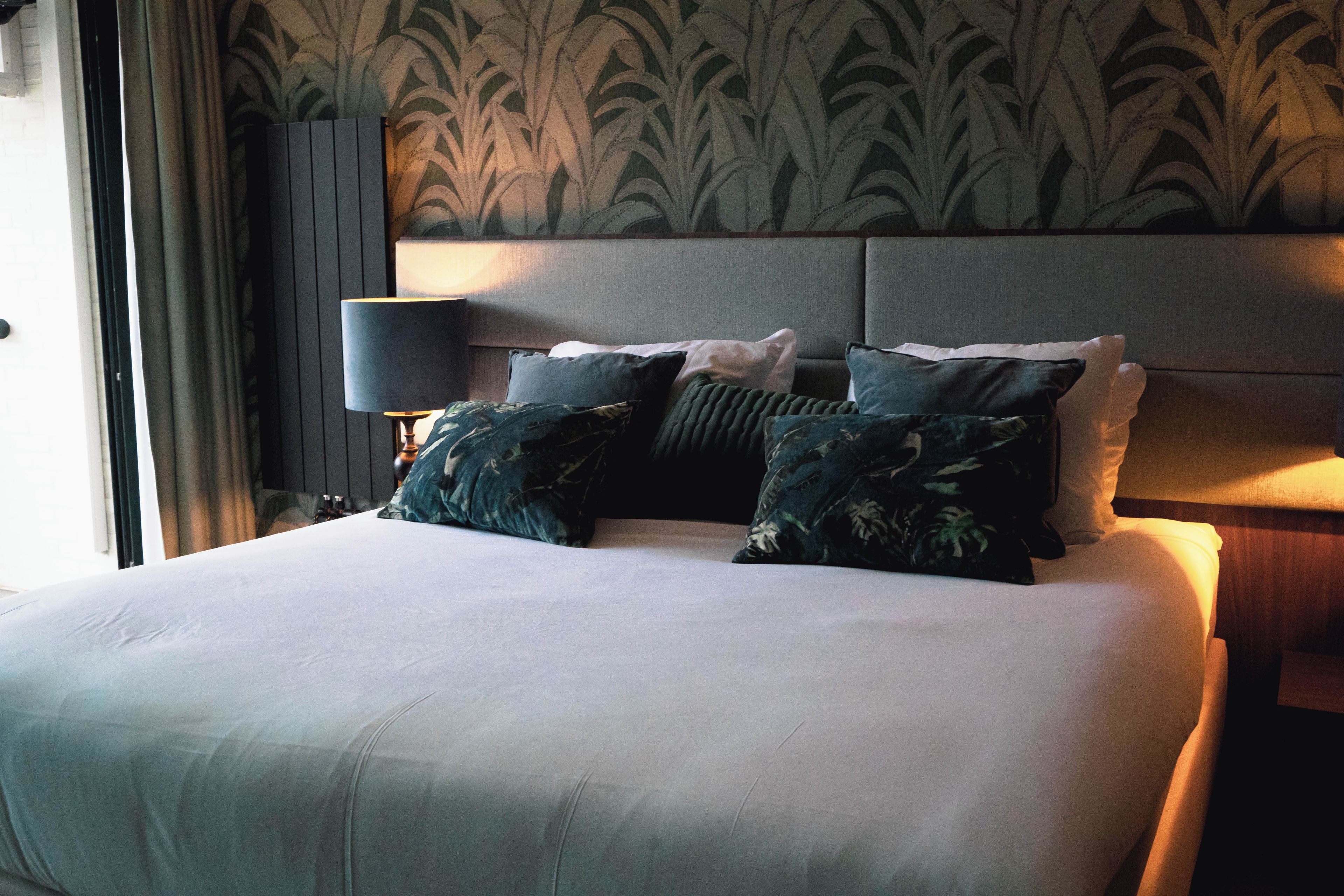 Habitación de hotel con una cama grande, una mesita de noche, una lámpara y un cabecero con un diseño de hojas.