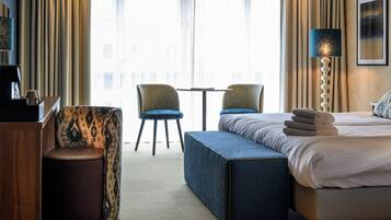A hotel room with a bed, two chairs, a small table, a coffee machine, and a lamp.