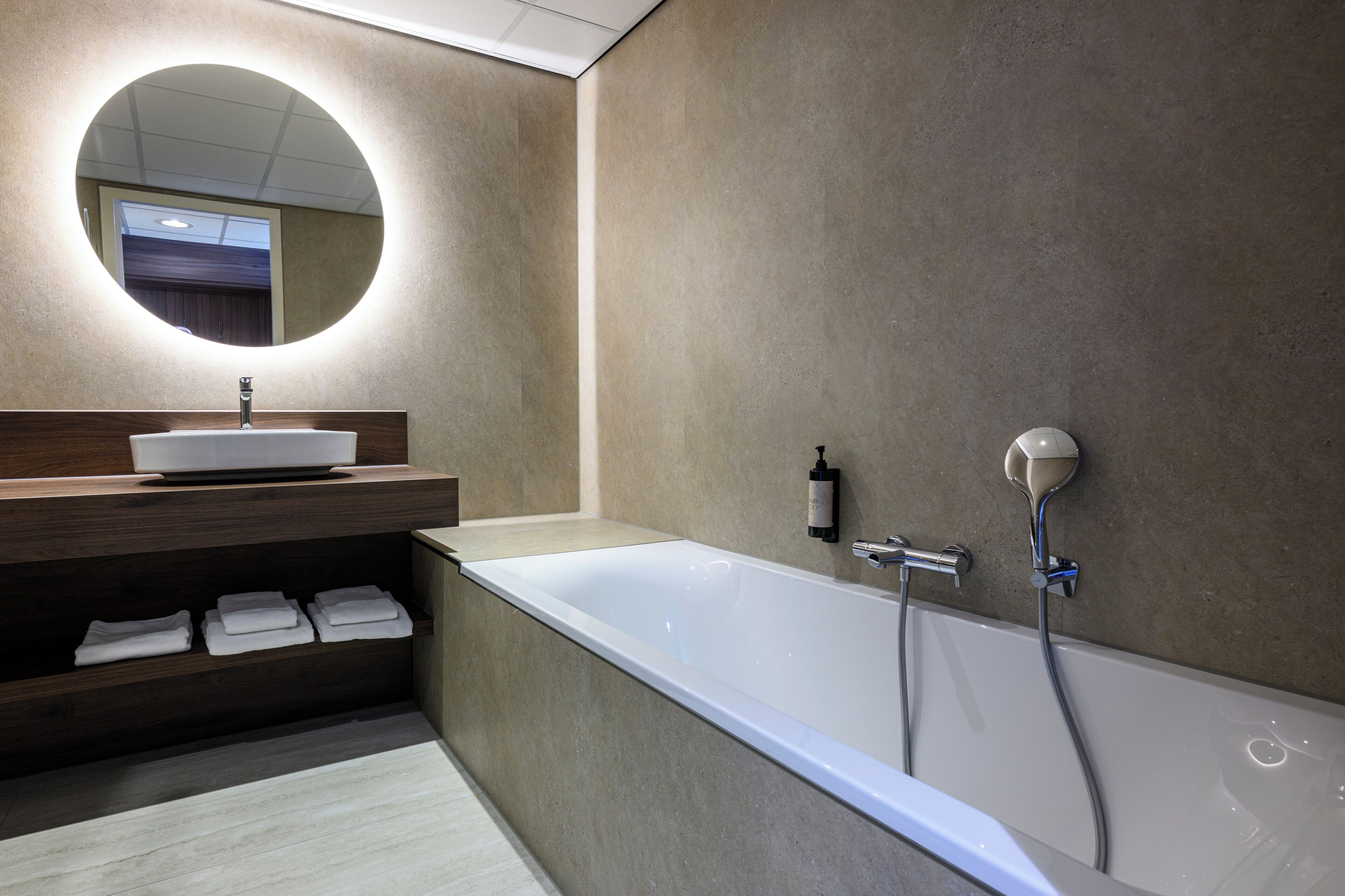 Un baño moderno con una bañera independiente, un espejo redondo y un mueble de tocador de madera con lavabo.