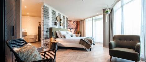 Un dormitorio moderno con una cama grande, una zona de estar con una silla y vistas al exterior a través de amplios ventanales.