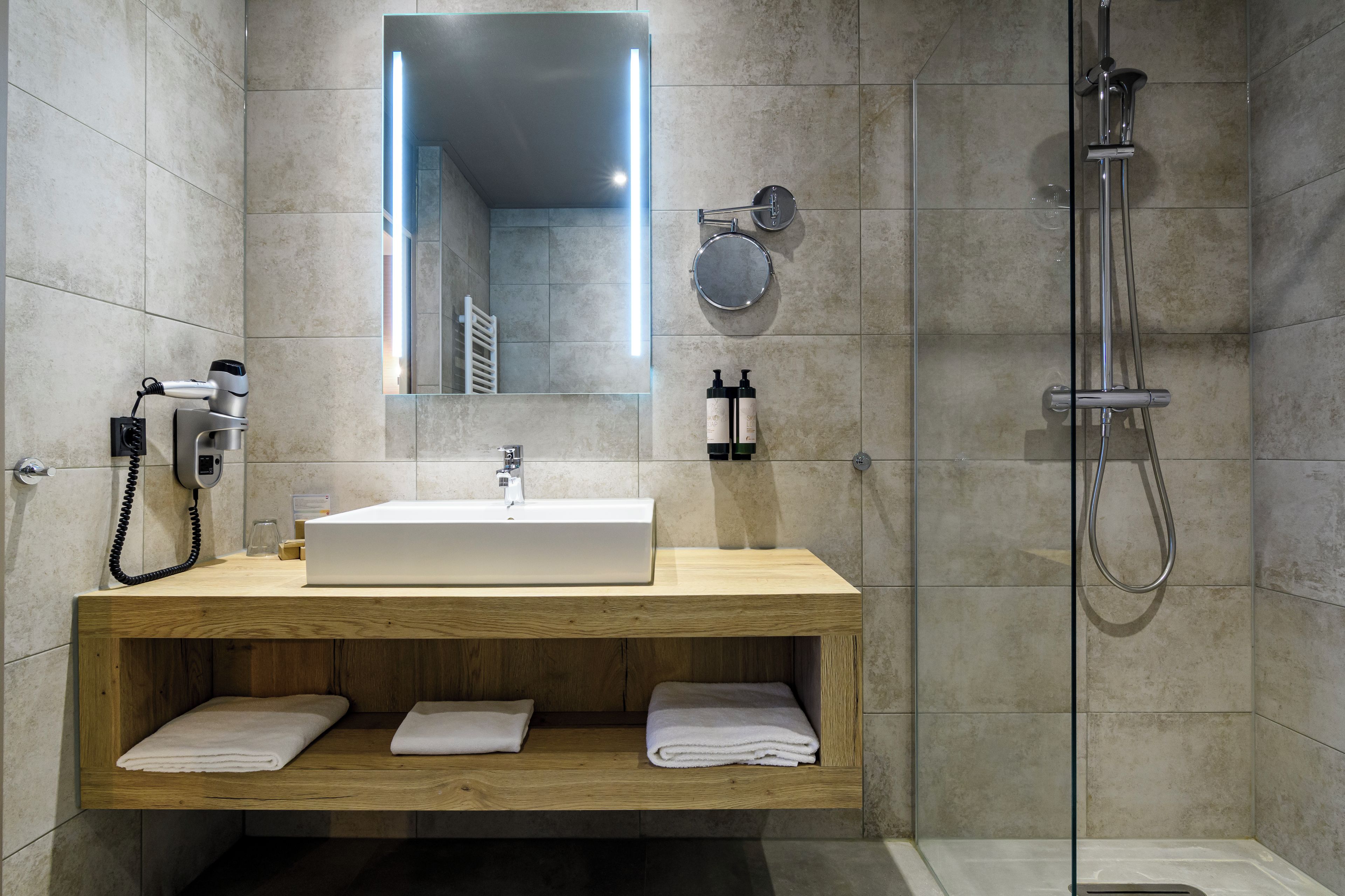 A modern bathroom with a built-in sink, a mirror, a handheld showerhead, and a towel rack.