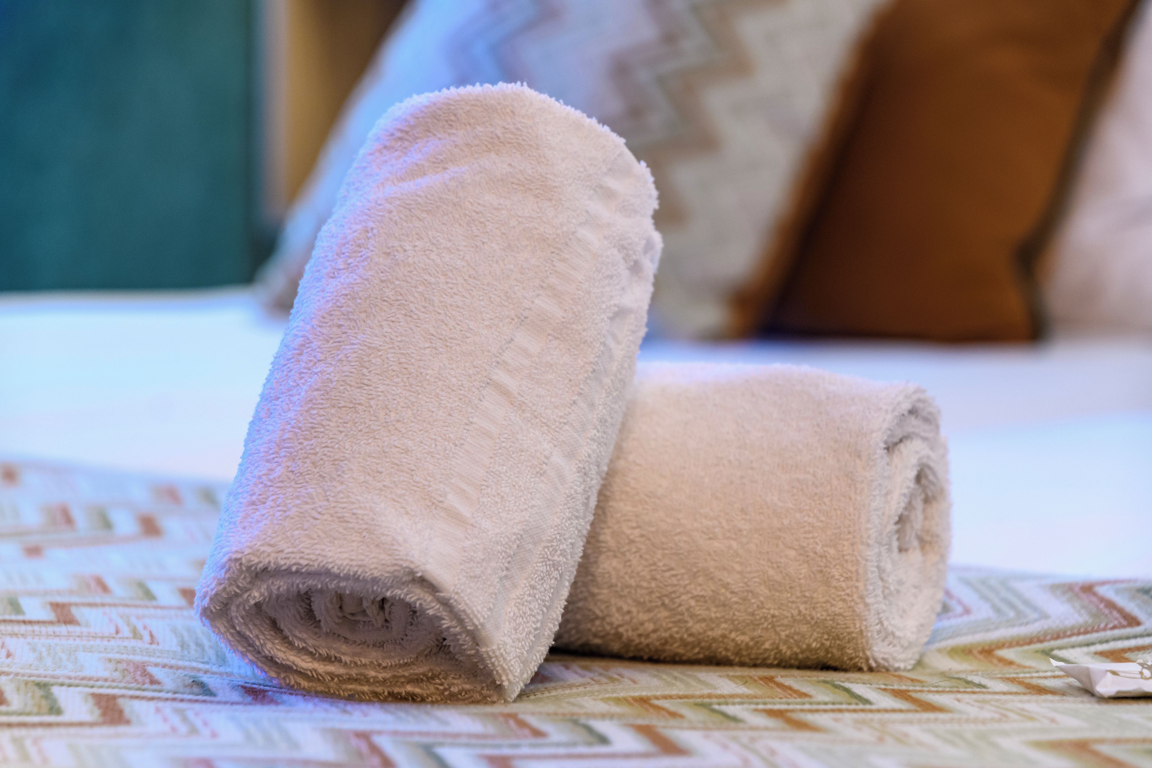 Two rolled towels on a bed with a patterned bedspread.
