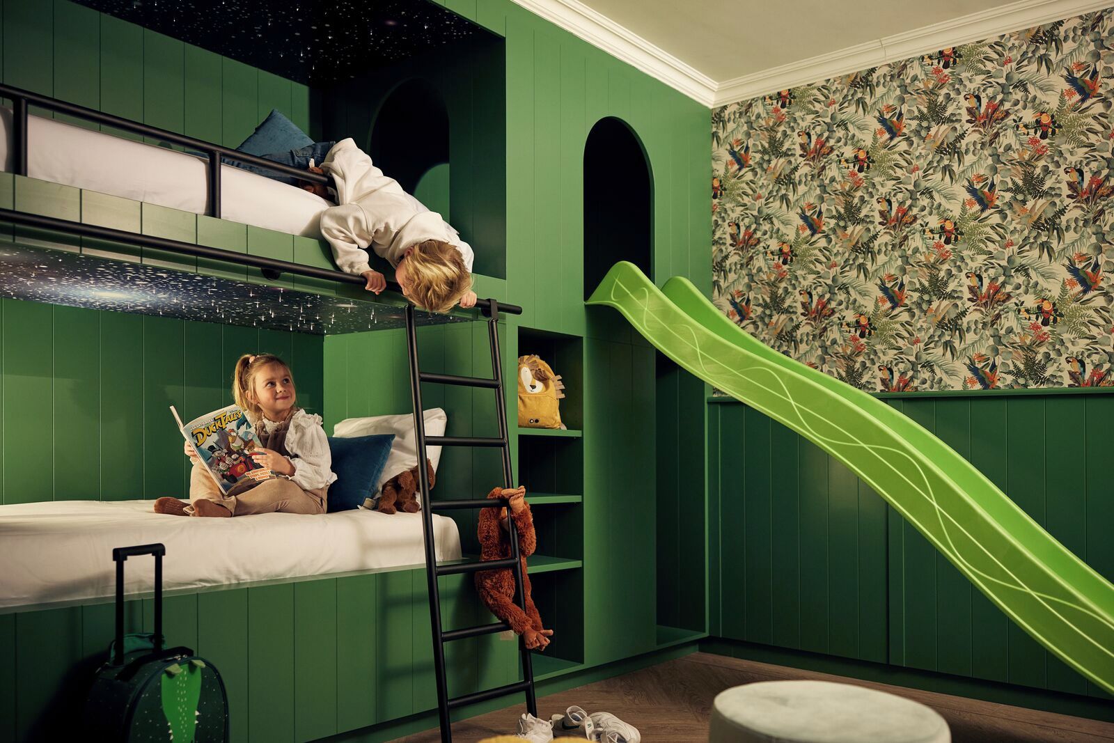 Habitación con literas, un tobogán verde, techo estrellado y papel tapiz floral.