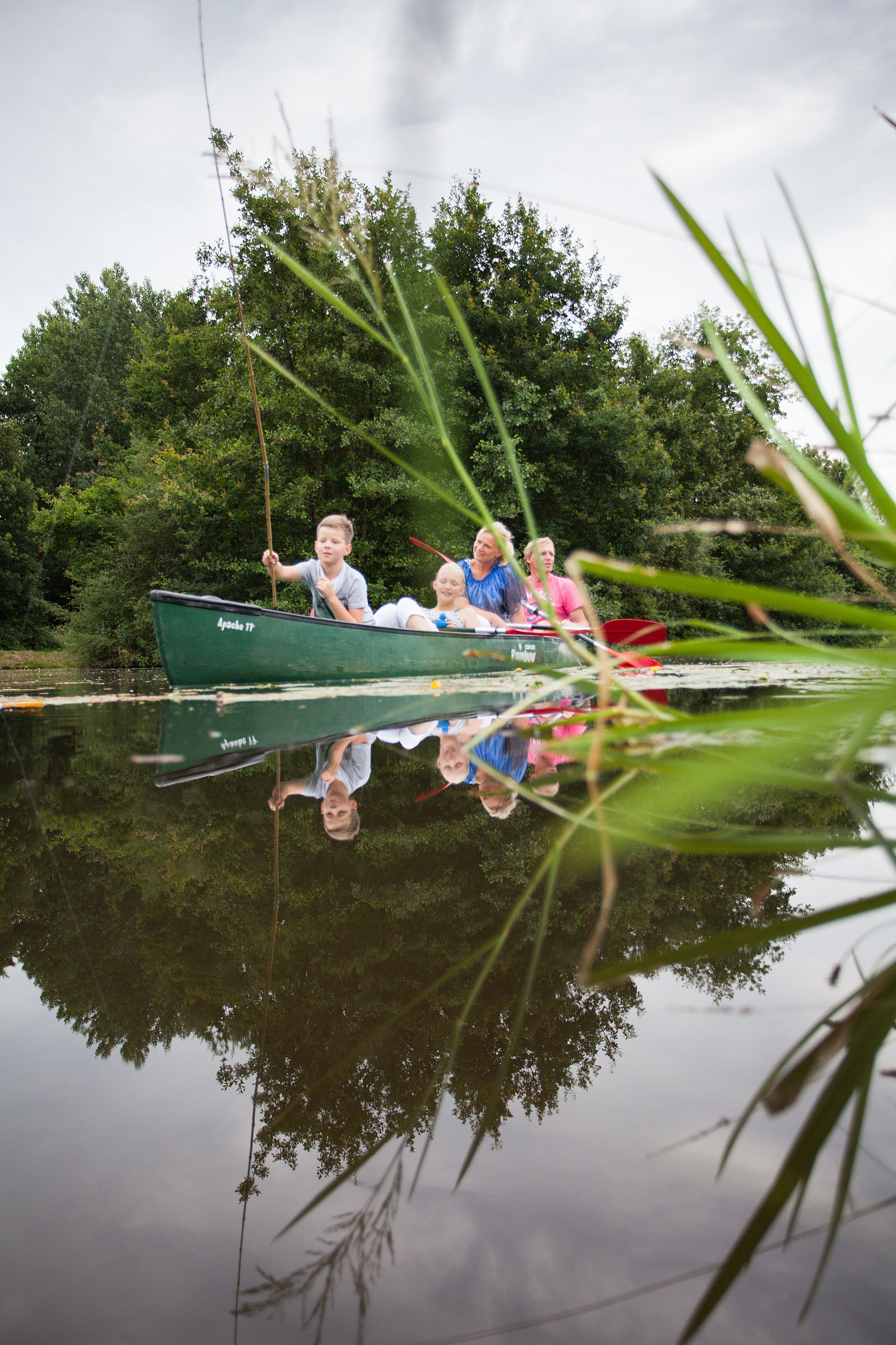 A green boat with people on it, reflecting in the water.
