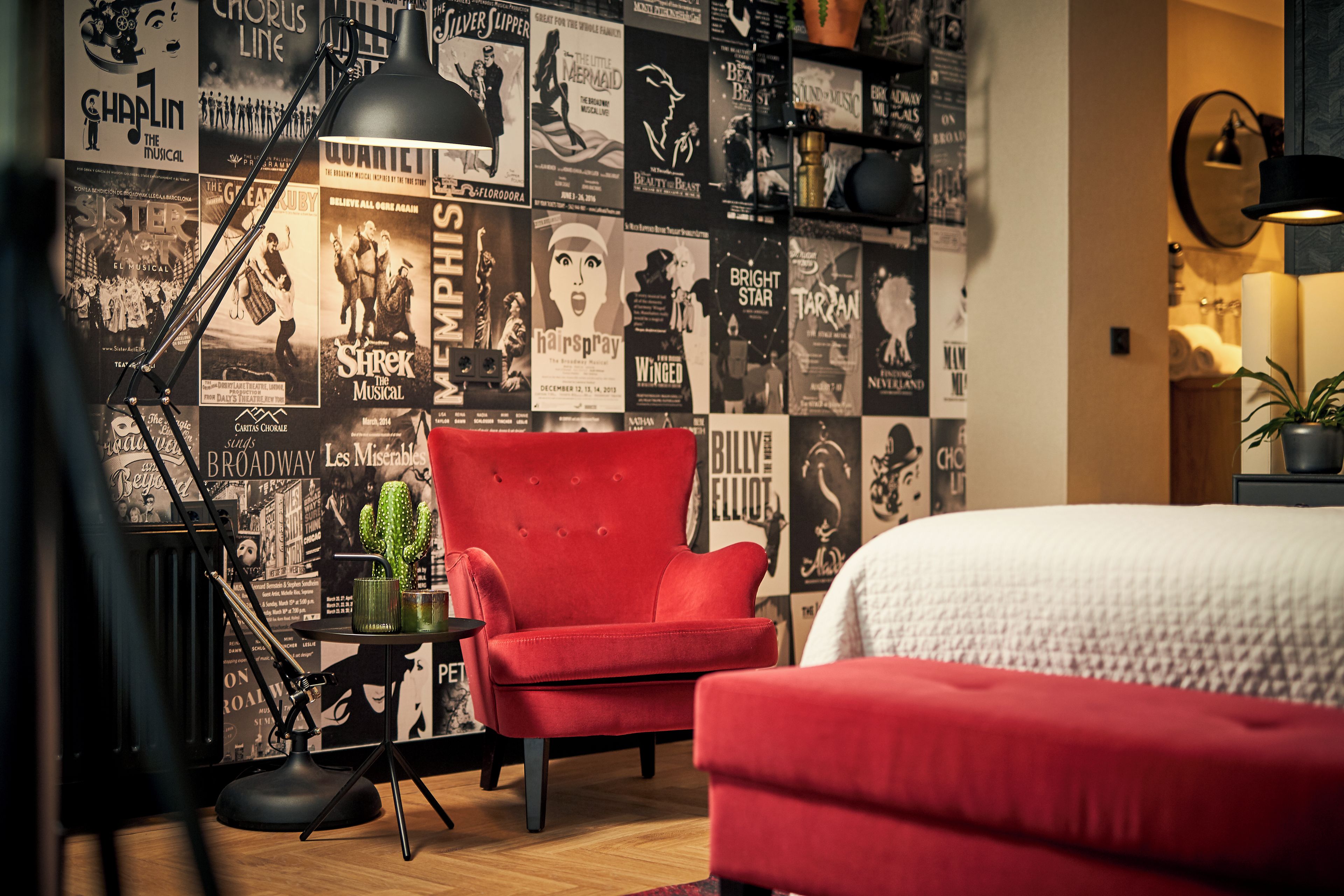 Una habitación con un sillón rojo, una cama y una pared decorada con carteles.