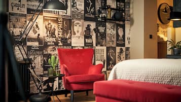Una habitación con un sillón rojo, una cama y una pared decorada con carteles.