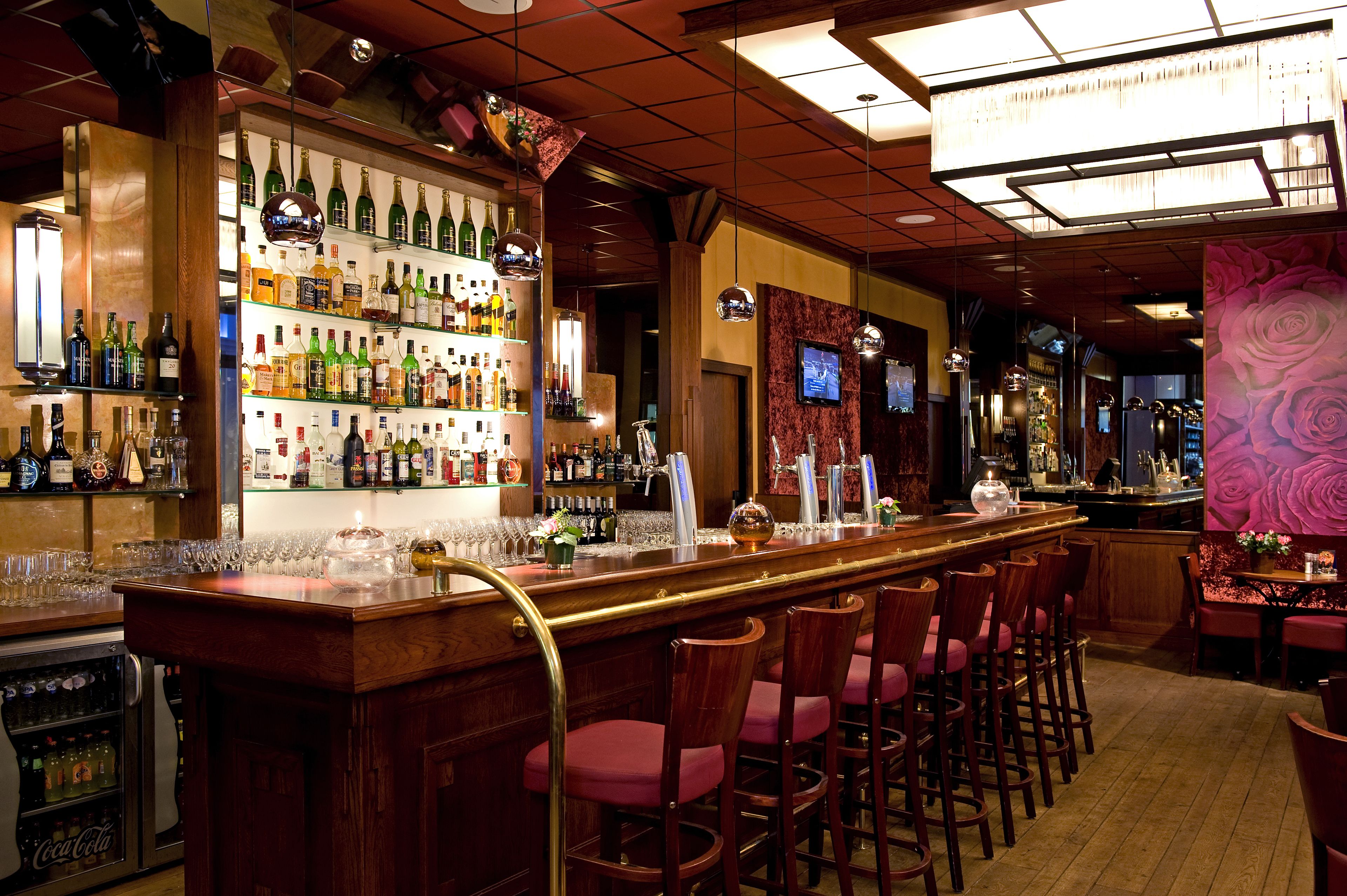 Zona de bar con varias estanterías llenas de botellas, una barra y varios taburetes.