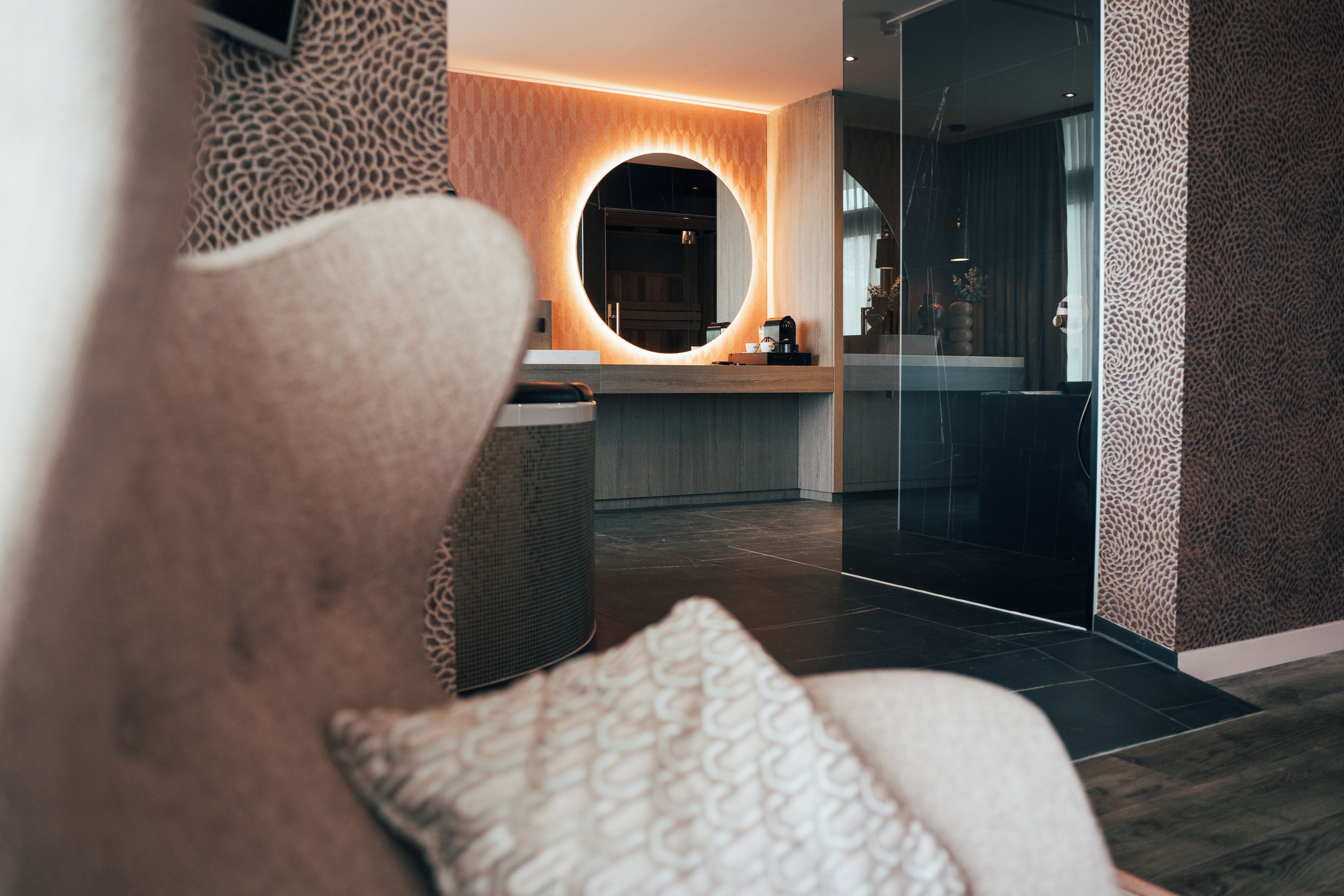 Ein modernes Interieur mit einer Rezeption, einem runden Spiegel und einer Sitzecke mit gemustertem Kissen.