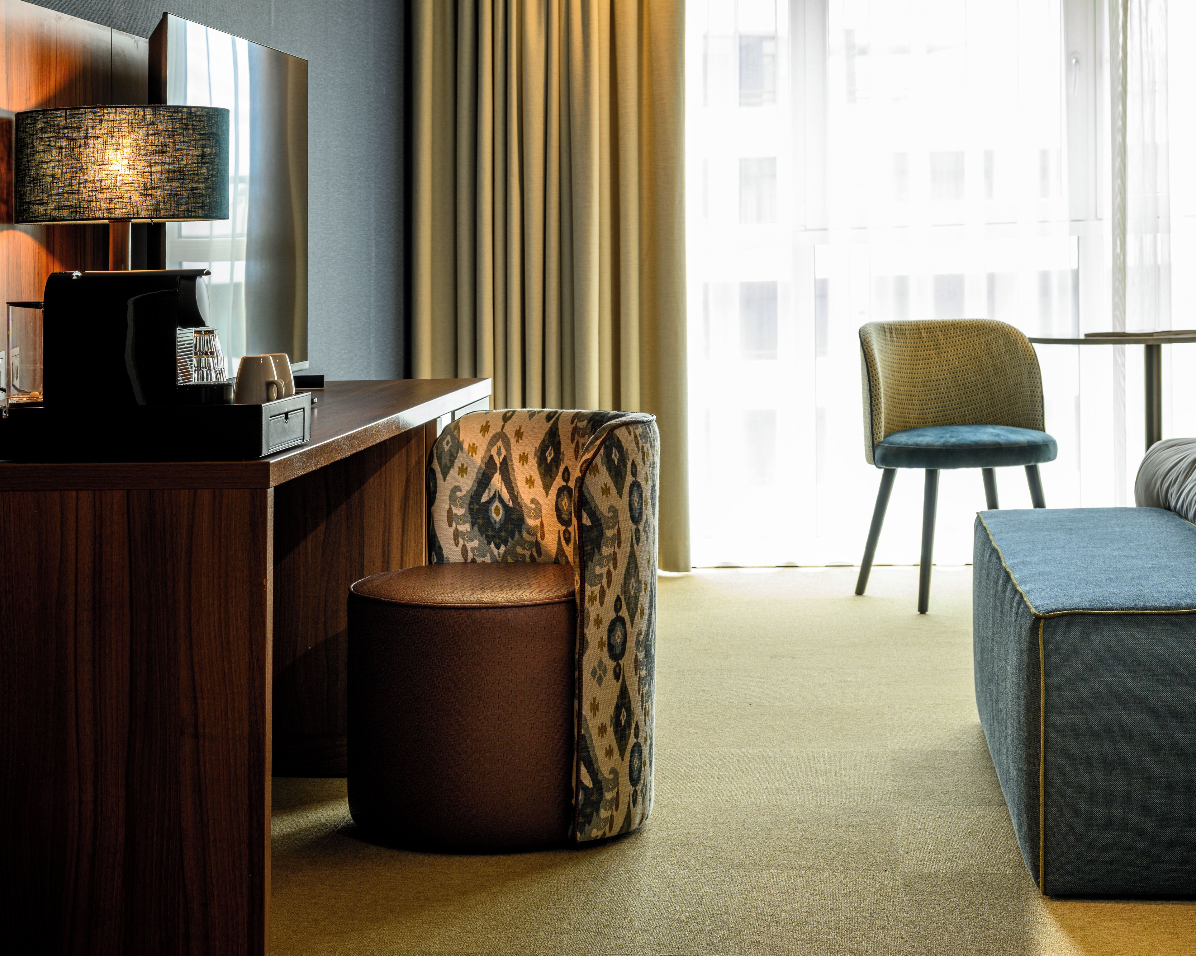 Habitación de hotel con escritorio, una silla, sofá y una ventana grande con cortinas.