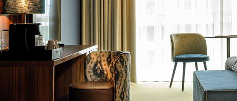 Habitación de hotel con escritorio, una silla, sofá y una ventana grande con cortinas.