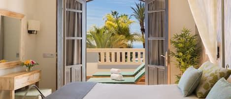 A hotel room with a bed, a vanity with a mirror, a small table with a towel, and a view of the outdoors.
