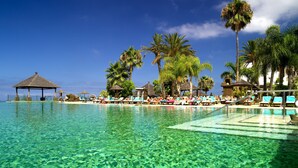 A clear pool with lounge chairs and palm trees.