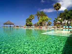 A clear pool with lounge chairs and palm trees.