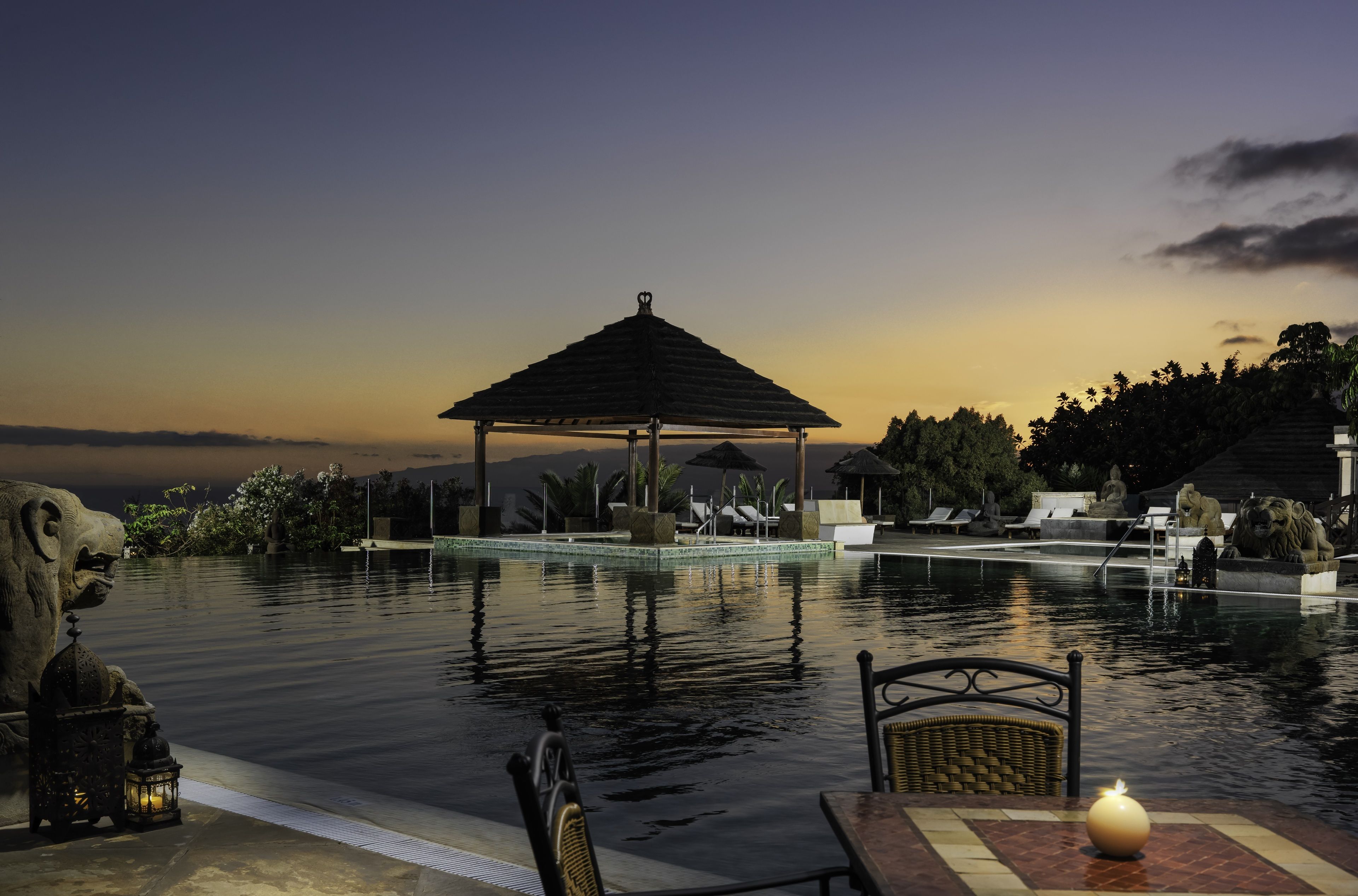 A serene pool area with a gazebo, lounge chairs, and a statue.