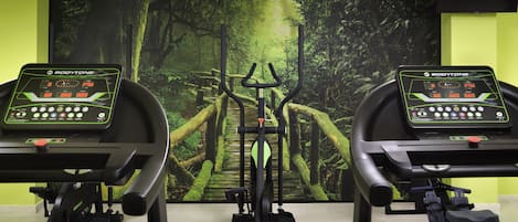 Two stationary bikes with digital displays, set against a forest-themed backdrop.