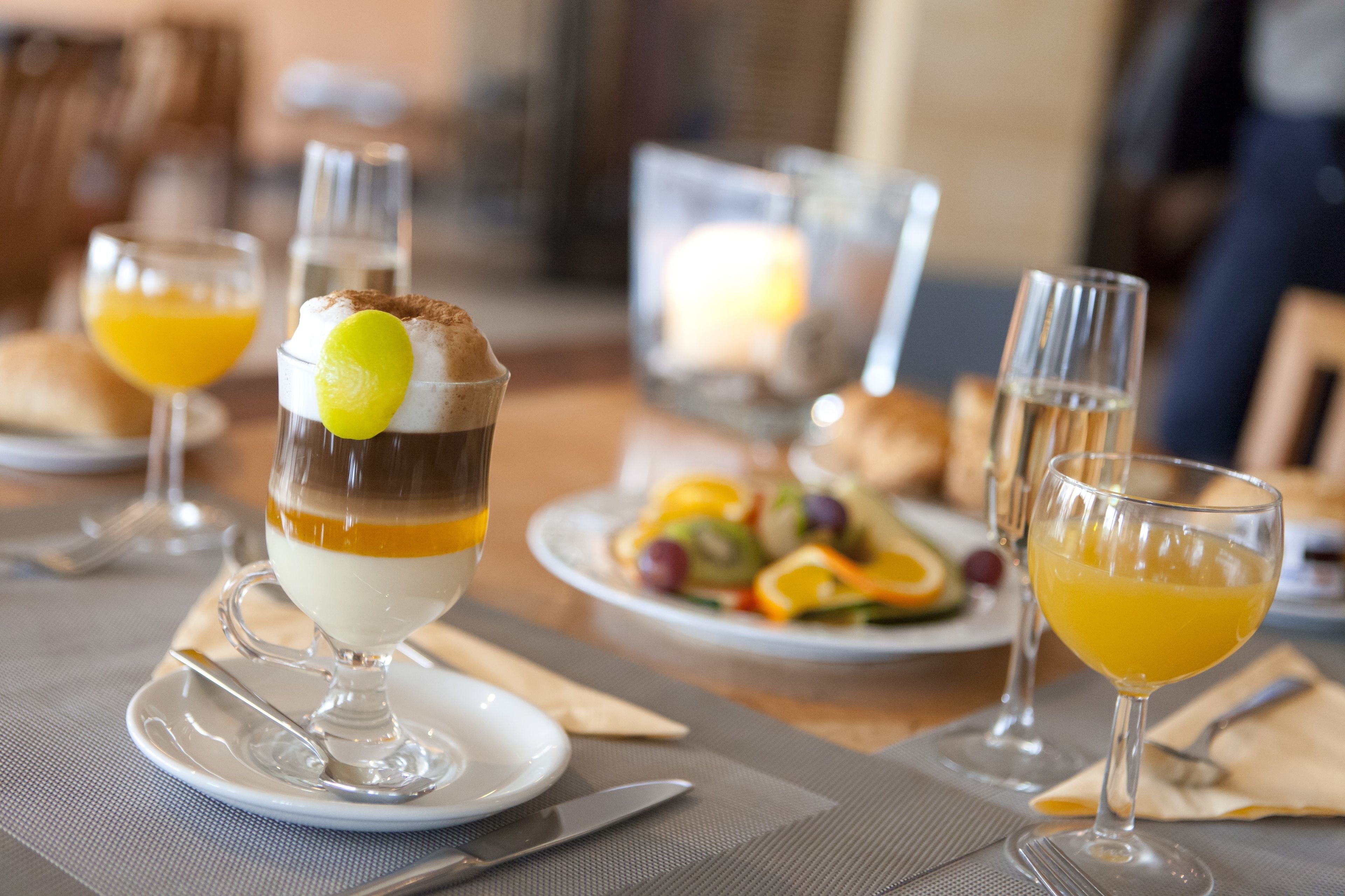 A dining table with a dessert, a fruit drink, and a plate of fruit salad.