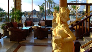 A luxurious lobby with wicker furniture, a statue, and a view of a pool and resort buildings. - Regency Country Club, Apartments Suites (Arona)