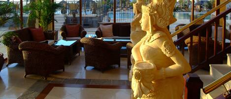 A luxurious lobby with wicker furniture, a statue, and a view of a pool and resort buildings.