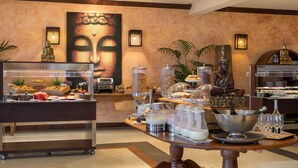 A buffet area with various food items, a Buddha statue, and a large Buddha painting on the wall.