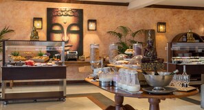A buffet area with various food items, a Buddha statue, and a large Buddha painting on the wall.