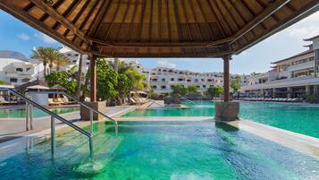 Una piscina con sillas de descanso y una zona cubierta, rodeada de edificios con balcones.