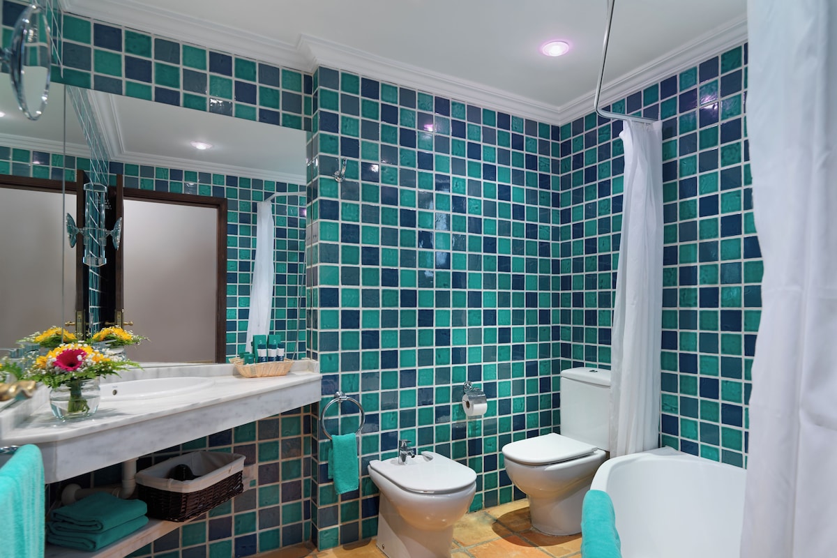 A bathroom with a tiled wall, a sink, a toilet, and a bathtub.