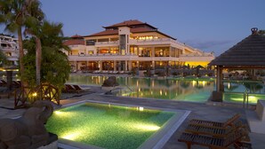 A resort with a large pool area, multiple lounge chairs, and a building with a traditional architectural style.