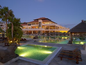 A resort with a large pool area, multiple lounge chairs, and a building with a traditional architectural style.
