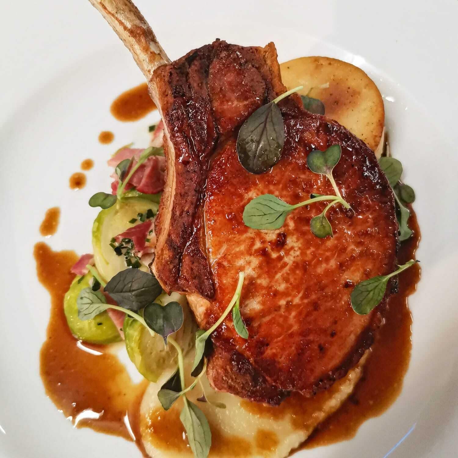 A plate of food with a lamb chop, potatoes, and greens.