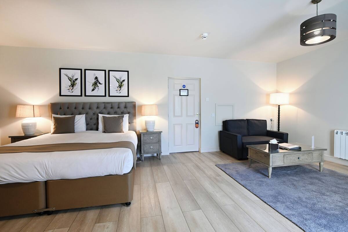 Ein modernes Hotelzimmer mit einem großen Bett, Nachttischlampen, einem Couchtisch, einer Couch und gerahmten Kunstwerken an der Wand.