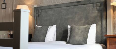 Una cama bien hecha con un cabecero tapizado gris, ropa de cama blanca y dos almohadas grises.