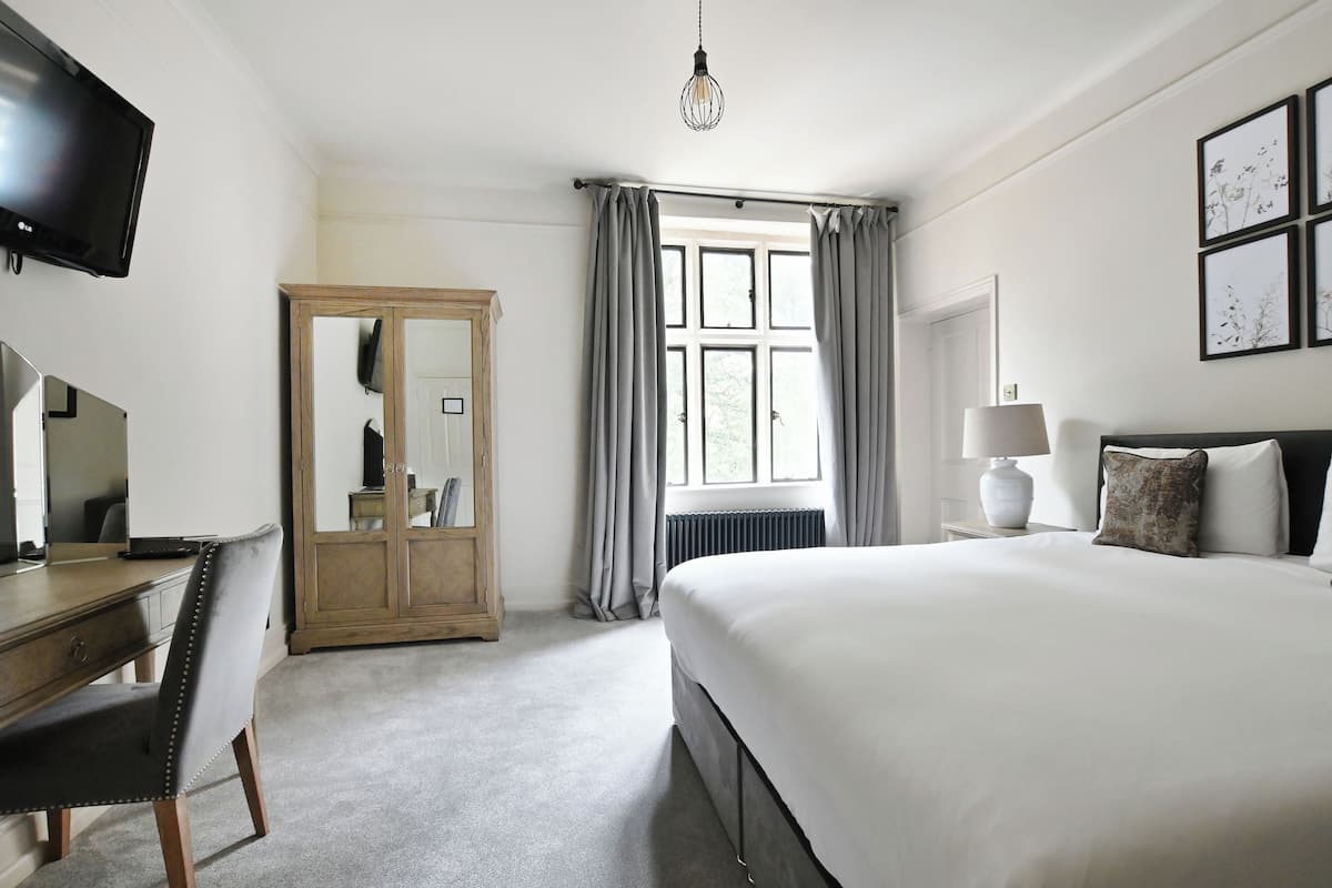 Ein Hotelzimmer mit Bett, Schreibtisch, Kleiderschrank, Fernseher und einem fensterbepflanzten Fenster.