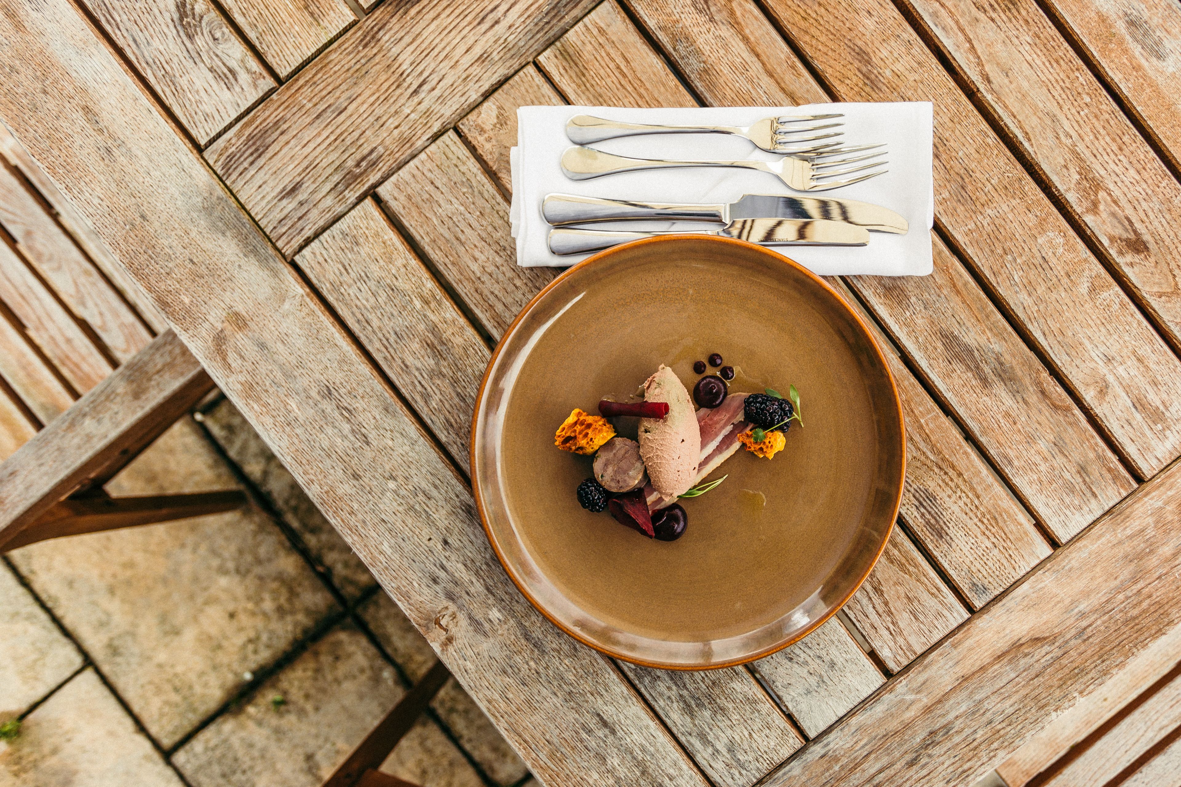 Una mesa de madera con un plato de comida y un mantel individual blanco con cubiertos.